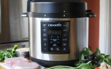 A crock pot sits on a counter with fish and veggies to the side
