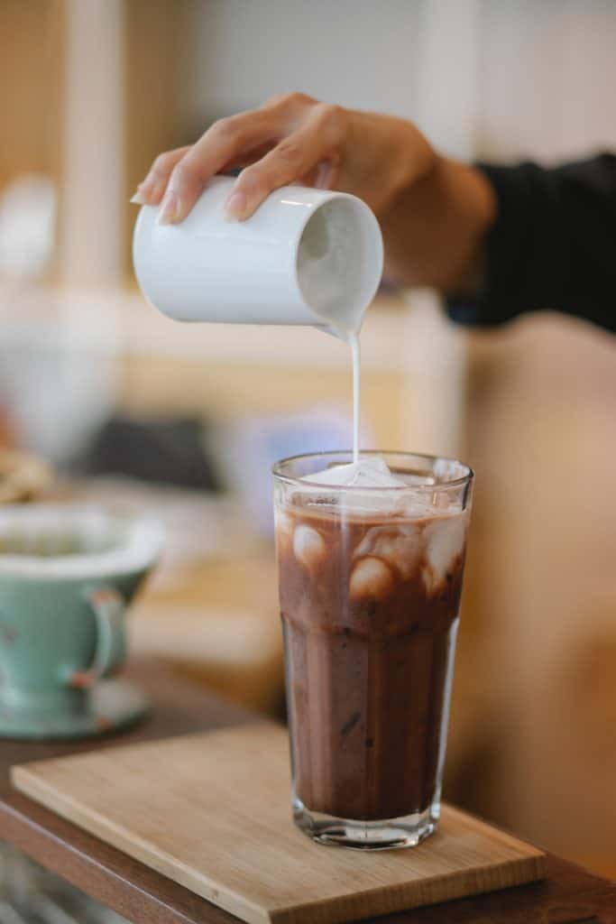 liquid coffee creamer being poured into iced coffee