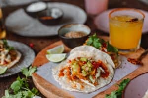 taco on flour tortilla surrounded by toppings and drinks. 